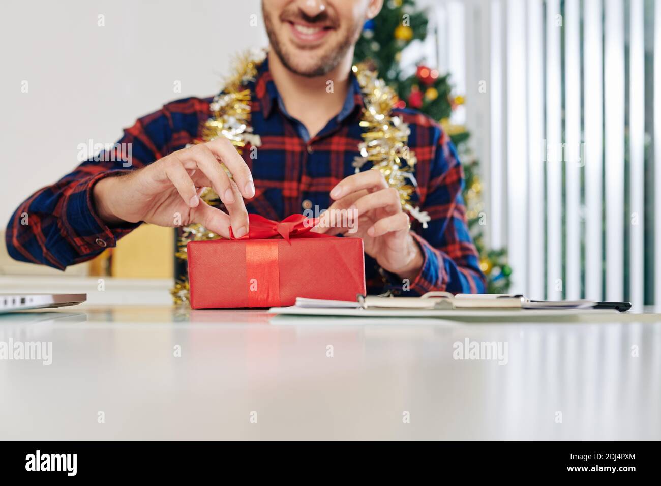 Un entrepreneur souriant et enthousiaste ouvre un cadeau de Noël à la réception Banque D'Images