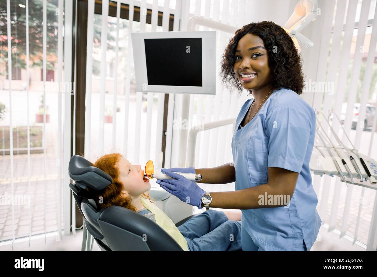 Médecine, stomatologie et soins dentaires concept. Jeune femme africaine  souriante dentiste avec lampe UV à séchage dentaire, regardant la caméra,  dent de finition Photo Stock - Alamy