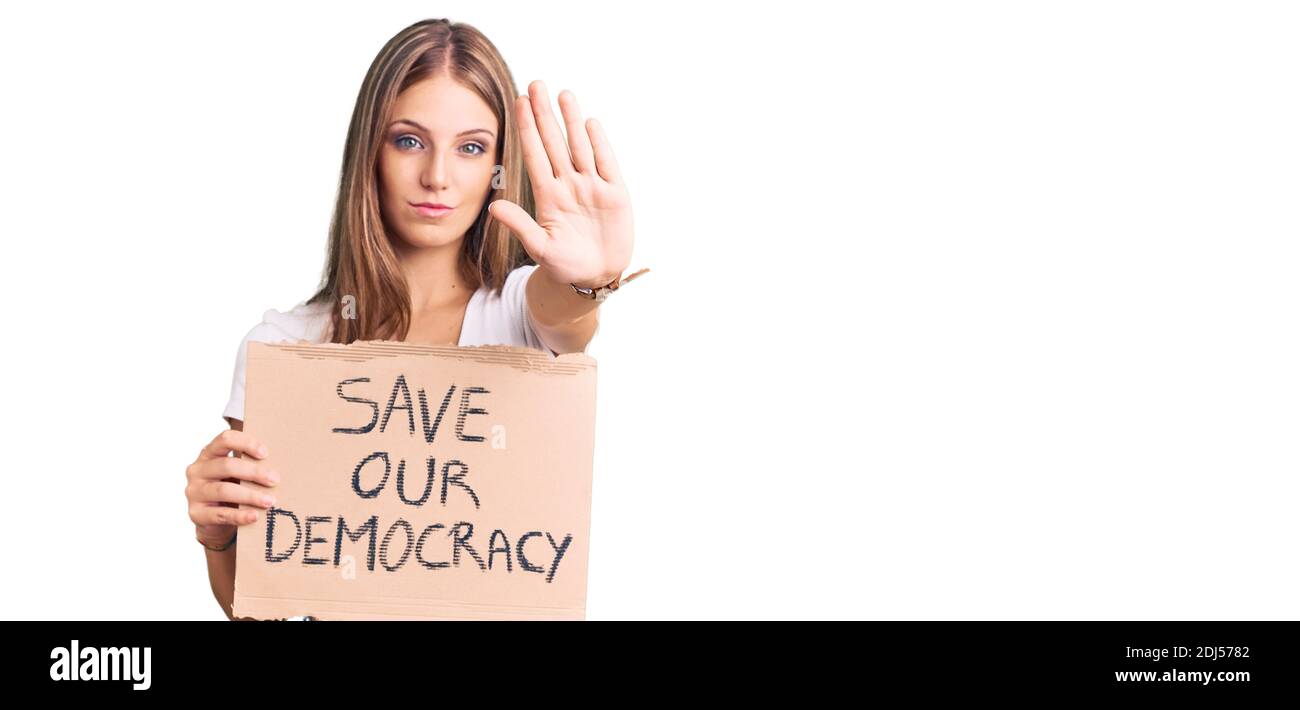 Jeune belle blonde tenue de sauver notre bannière de protestation de démocratie avec la main ouverte faisant signe d'arrêt avec une expression sérieuse et confiante, défense g Banque D'Images