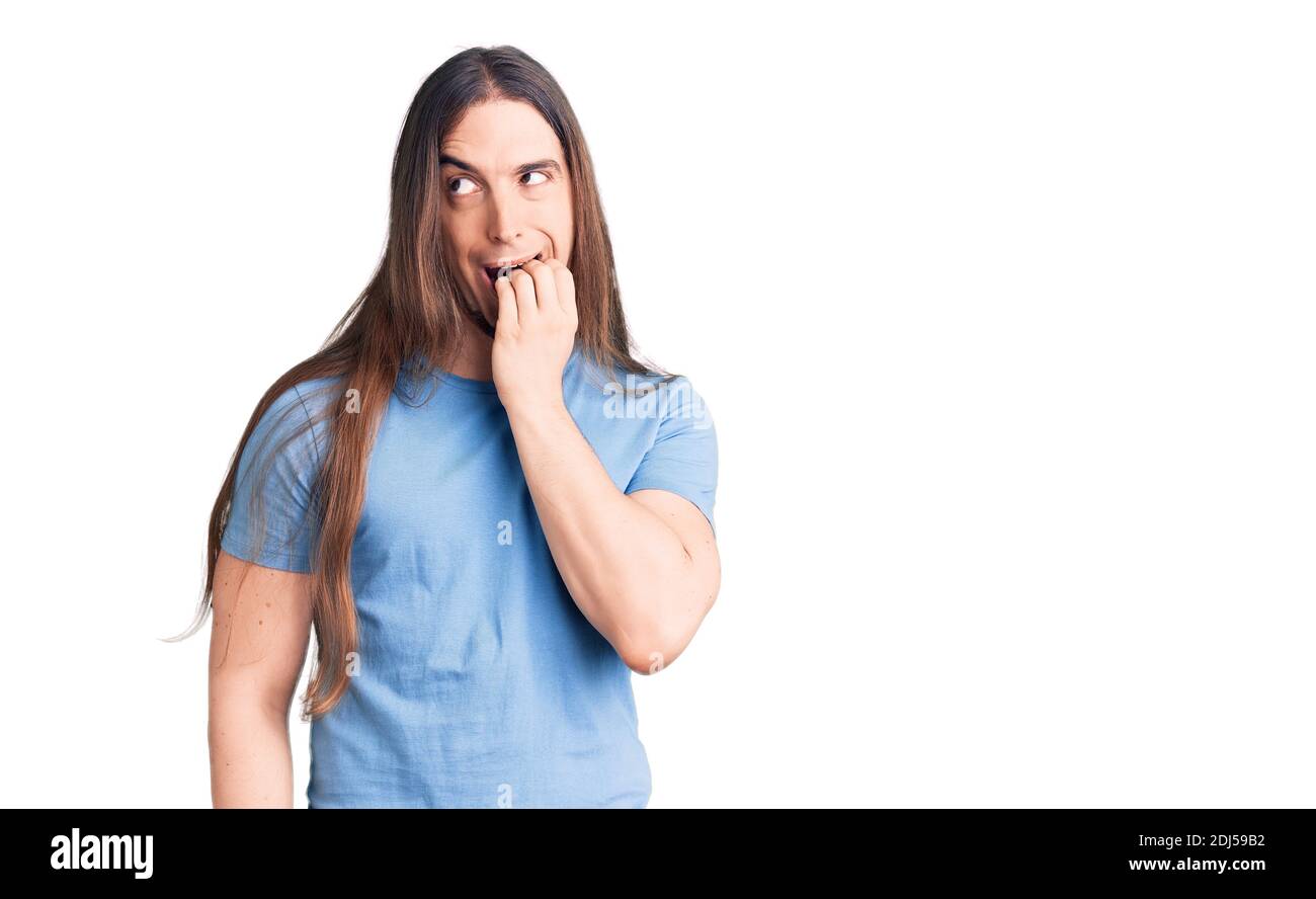 Jeune homme adulte avec de longs cheveux portant des vêtements décontractés ayant l'air stressé et nerveux avec les mains sur la bouche piquant les ongles. Problème d'anxiété. Banque D'Images