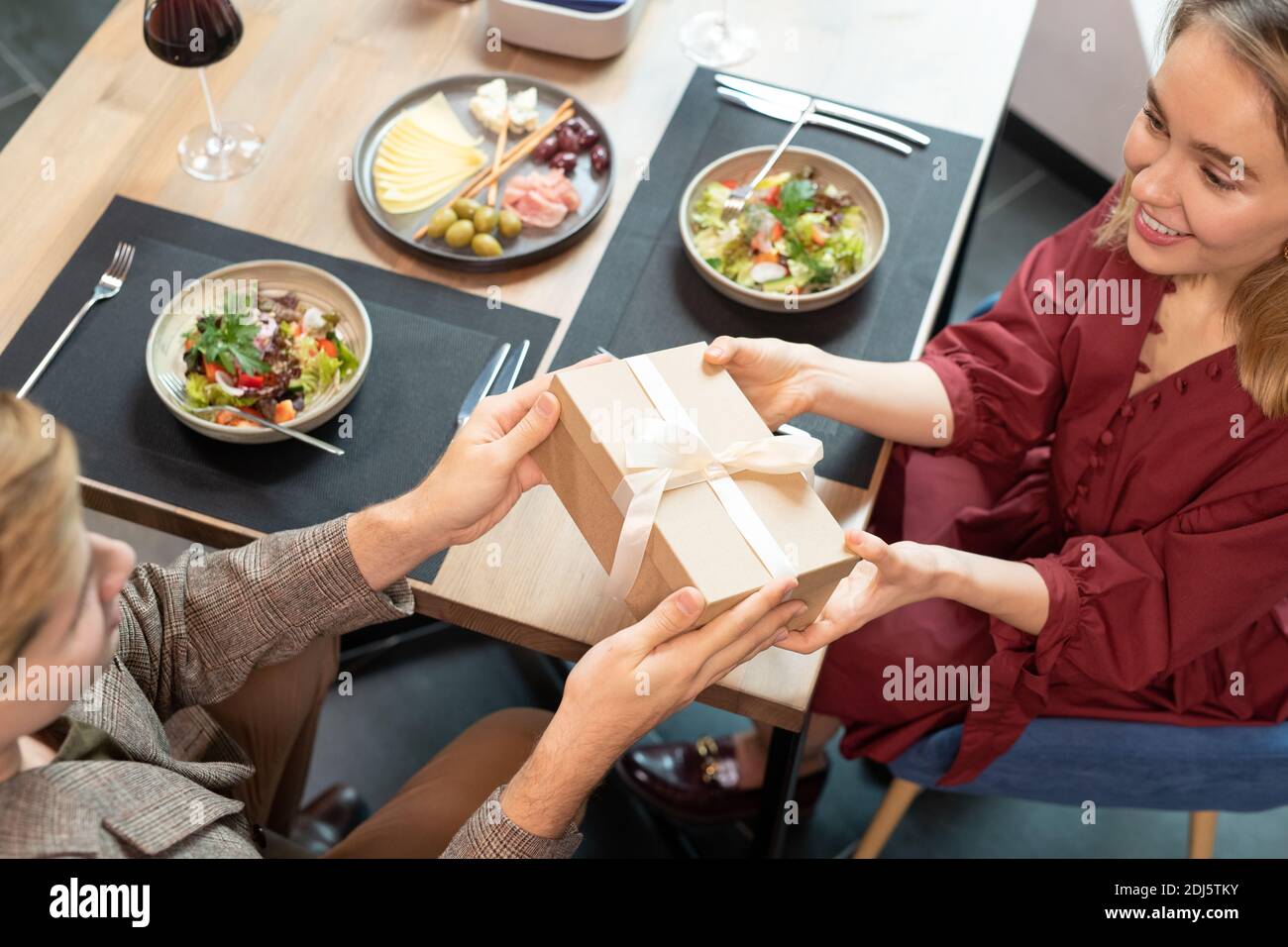Mains du jeune homme passant boîte-cadeau avec ruban de soie blanc à sa jolie petite fille tout en étant assis à la table de service et dîner ensemble Banque D'Images
