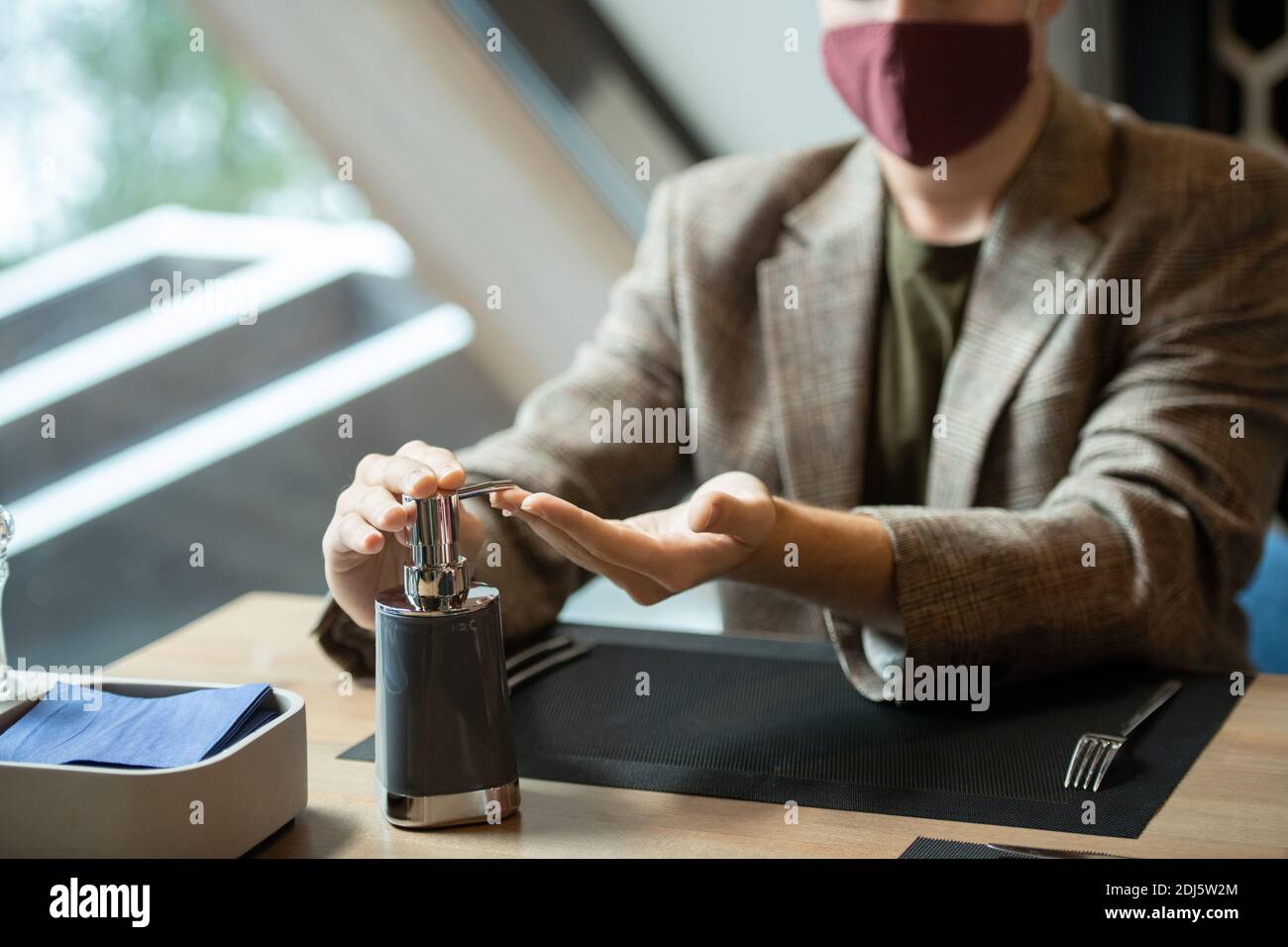 Mains de jeune homme contemporain distributeur de pression de pot en plastique avec de l'assainisseur avant de dîner assis près d'une table restaurant Banque D'Images