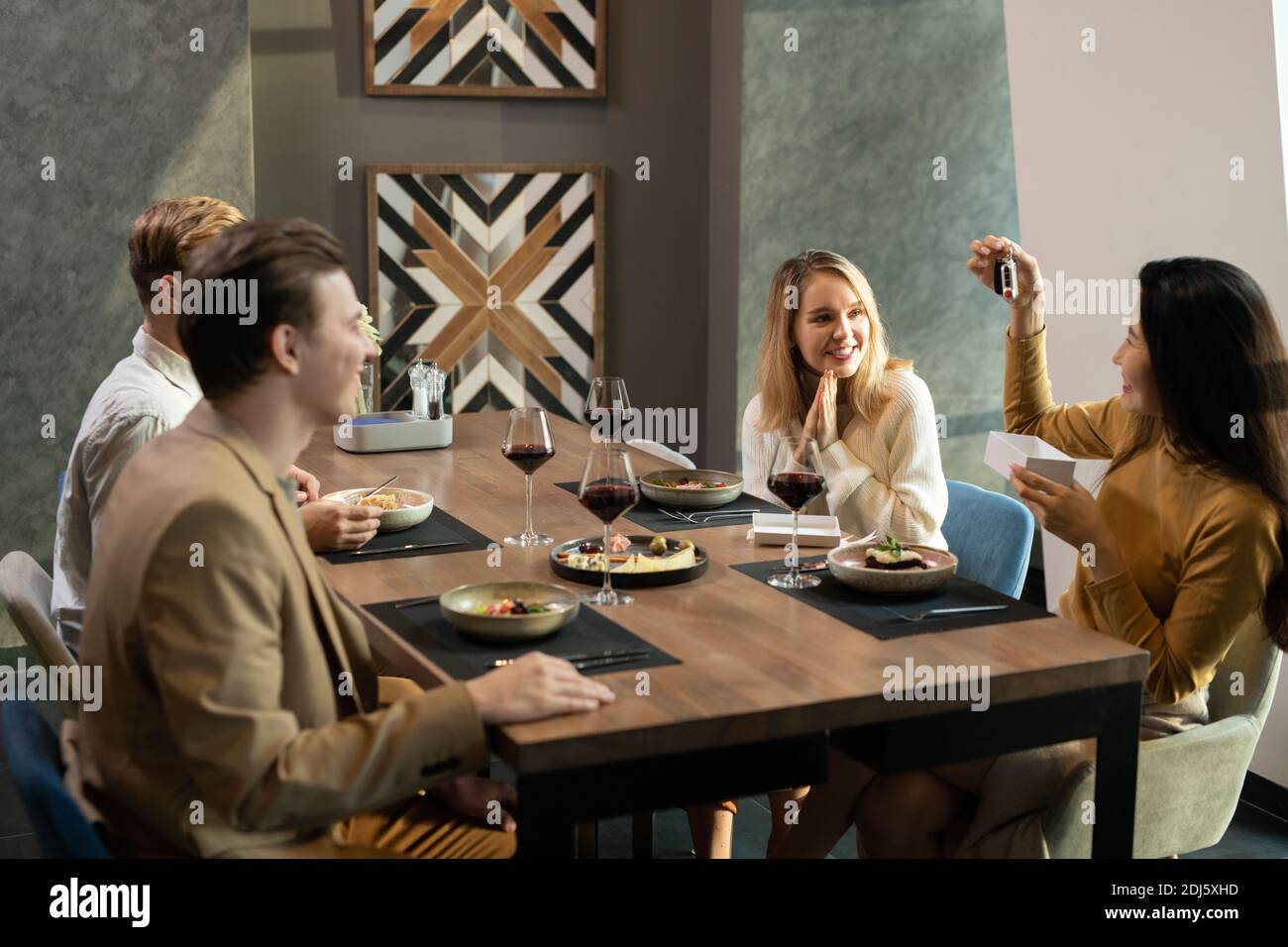 Jeune femme asiatique élégante avec une petite boîte cadeau vide qui la montre présentez-le à vos amis lors d'un dîner assis près d'une table de service dans un restaurant confortable Banque D'Images