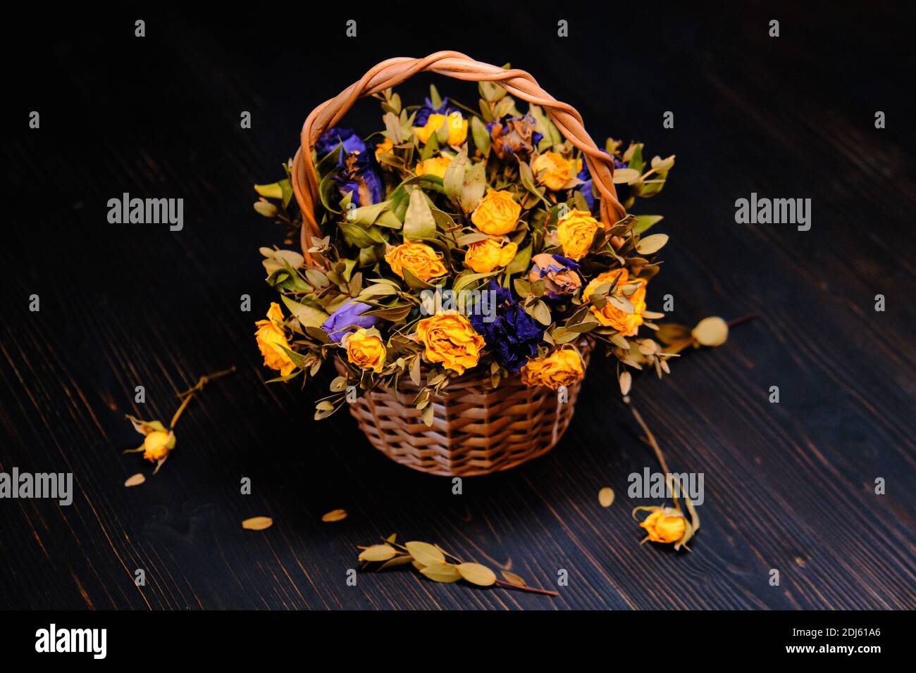 Panier avec roses jaunes et violets sèches. Bouquet de fleurs flétries sur fond de bois noir. Roses jaunes et bleues séchées en composition d'automne. Banque D'Images