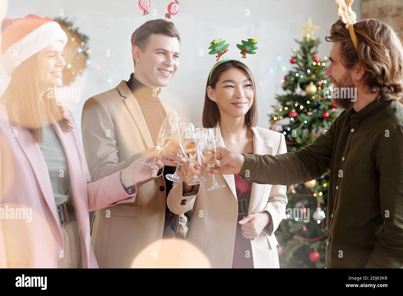 Joyeux jeunes collègues dans des bandeaux de Noël clinking avec des flûtes de champagne tout en faisant des toasts pour Noël lors d'une fête d'entreprise Banque D'Images
