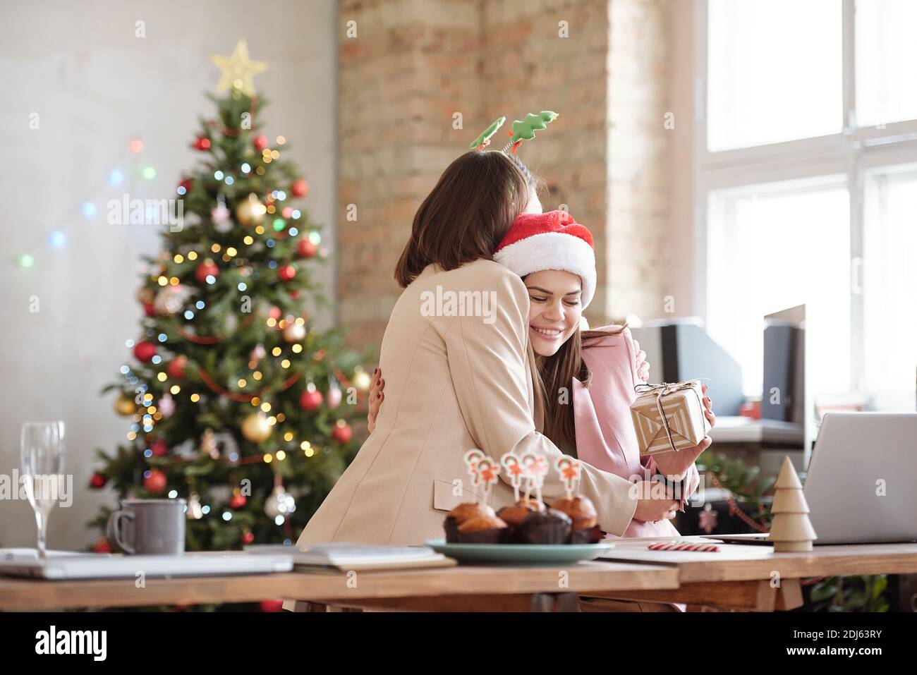 Une jeune femme d'affaires heureuse donne un câlin à sa collègue pendant Offrir un cadeau de Noël lors d'une fête d'entreprise dans un environnement de bureau Banque D'Images