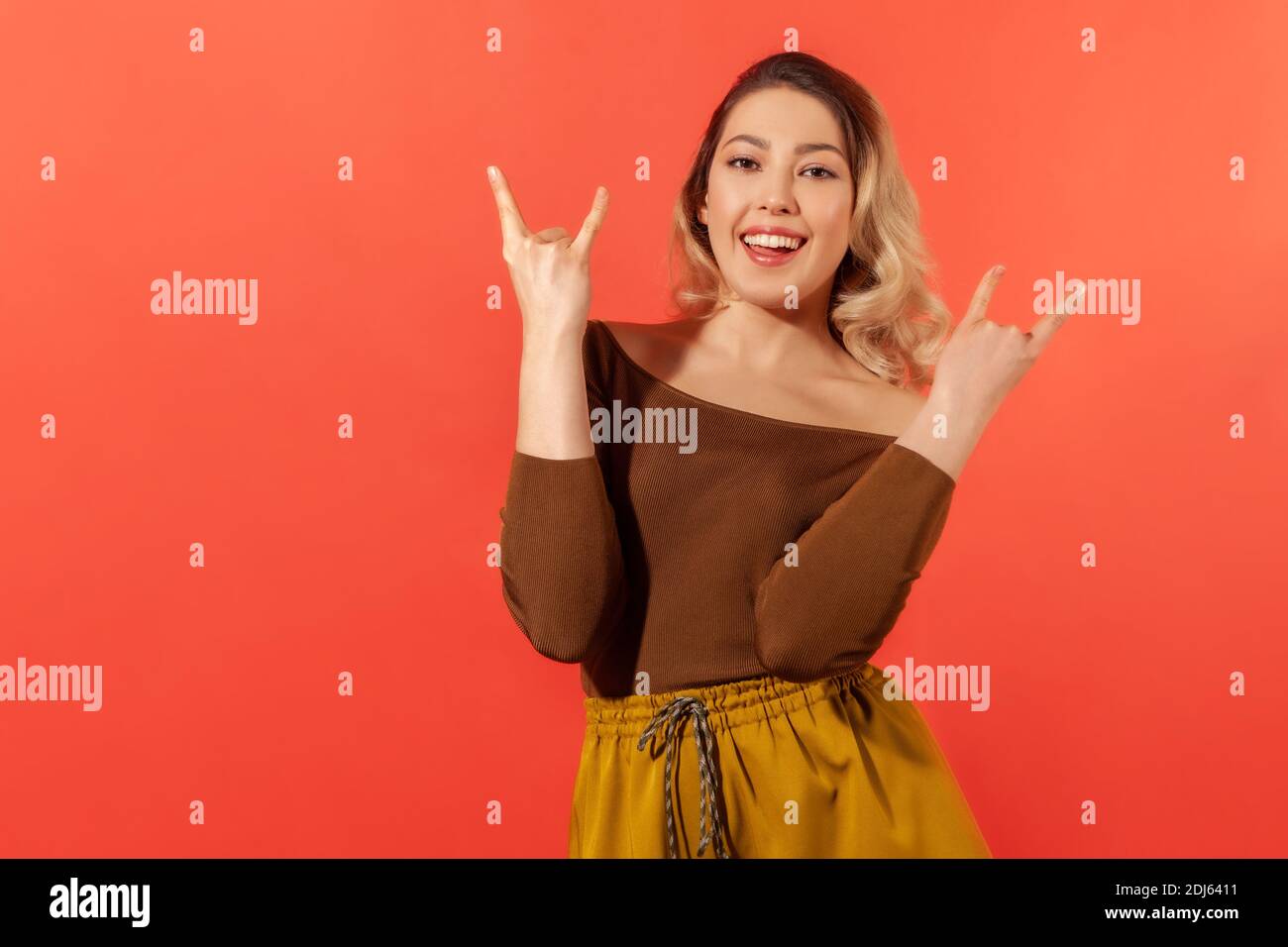 Oui, c'est génial ! Portrait d'une femme joyeuse dans un chemisier marron, se sentant fou, montrant des cornes de diable, le mouvement de la main de rock and roll, ravi du succès. Banque D'Images