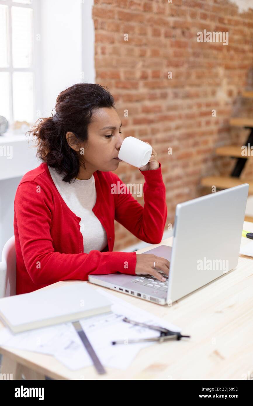Portrait d'une jeune femme brune qui a un café tout en travaillant à la maison avec son ordinateur portable. Espace pour le texte. Banque D'Images