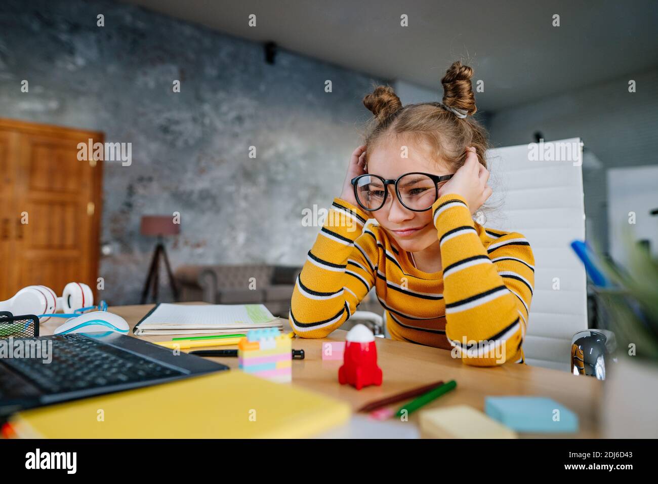 Fatigué 8 ans fille dans les lunettes étudiant en ligne de la maison en utilisant l'ordinateur portable assis au bureau dans la chambre. Formation à distance pendant le lockd pandémique Banque D'Images