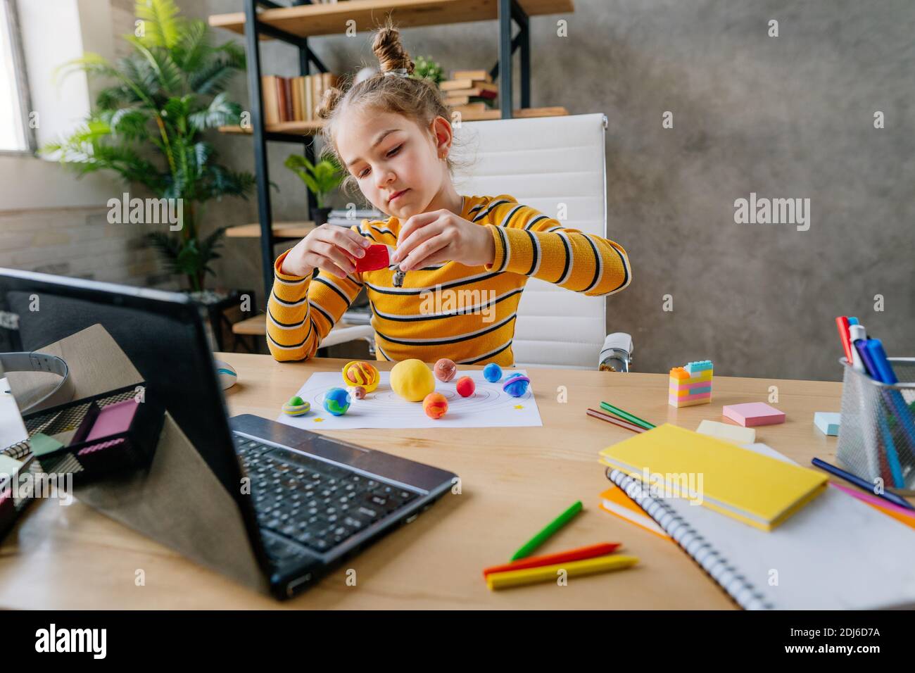 Petite fille de 8 ans utilisant un ordinateur portable pour étudier les planètes en ligne du système solaire assis au bureau dans la chambre. Jeune étudiante à l'école primaire W Banque D'Images