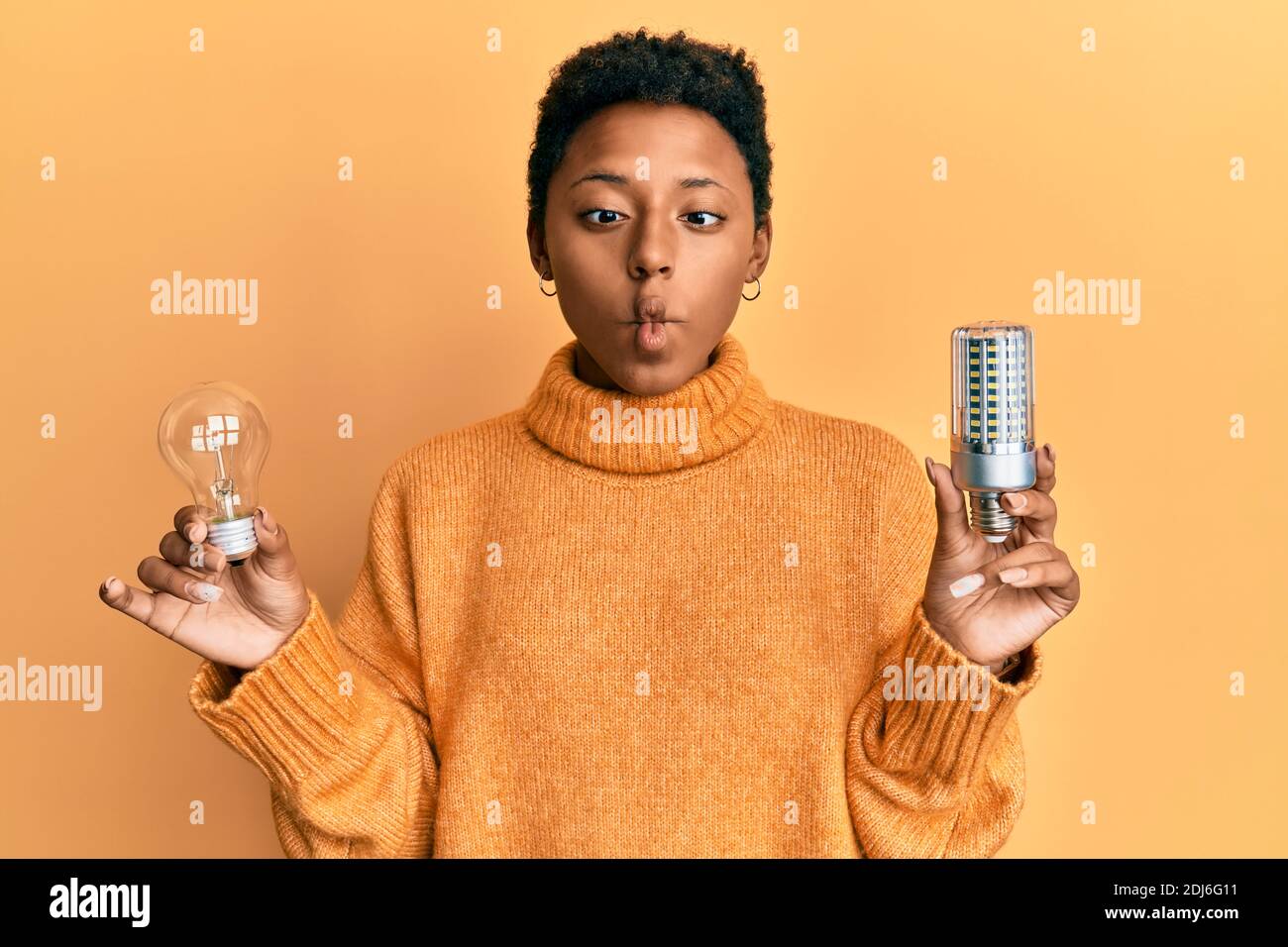 Jeune fille afro-américaine tenant une ampoule pour l'inspiration et l'idée de faire le visage de poisson avec la bouche et les yeux de bourdonner, fou et comique. Banque D'Images