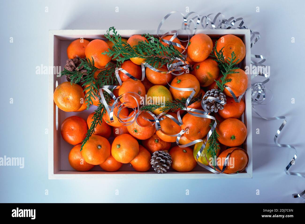 Boîte de mandarines décorée de branches de cyprès et de tingel sur une table blanche, vue du dessus. Concept Noël et nouvel an Banque D'Images