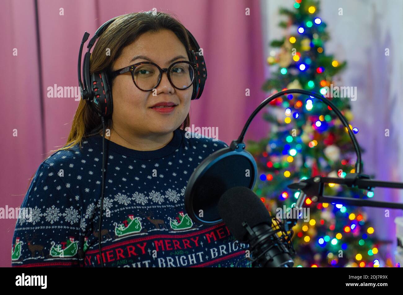 Une dame portant un pull de Noël et portant un casque chantant dans un microphone, enregistrant des voix pour une chanson. Banque D'Images