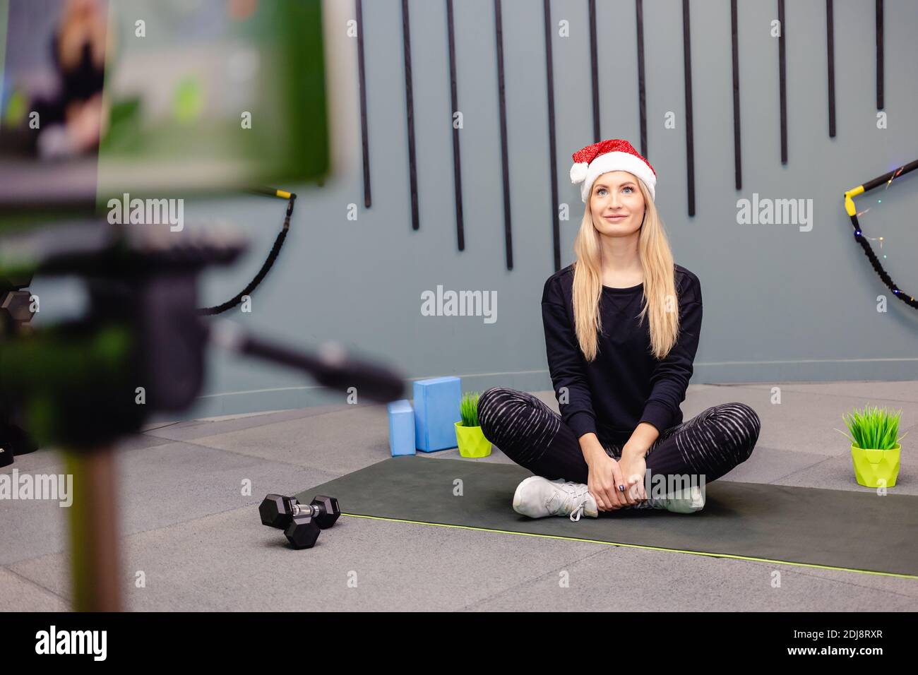 Une fille mince en chapeau de santa, tenue de sport enregistre des vidéos d'entraînement sur l'appareil photo. Blog sur le sport à la maison, tutoriel vidéo de fitness. Banque D'Images