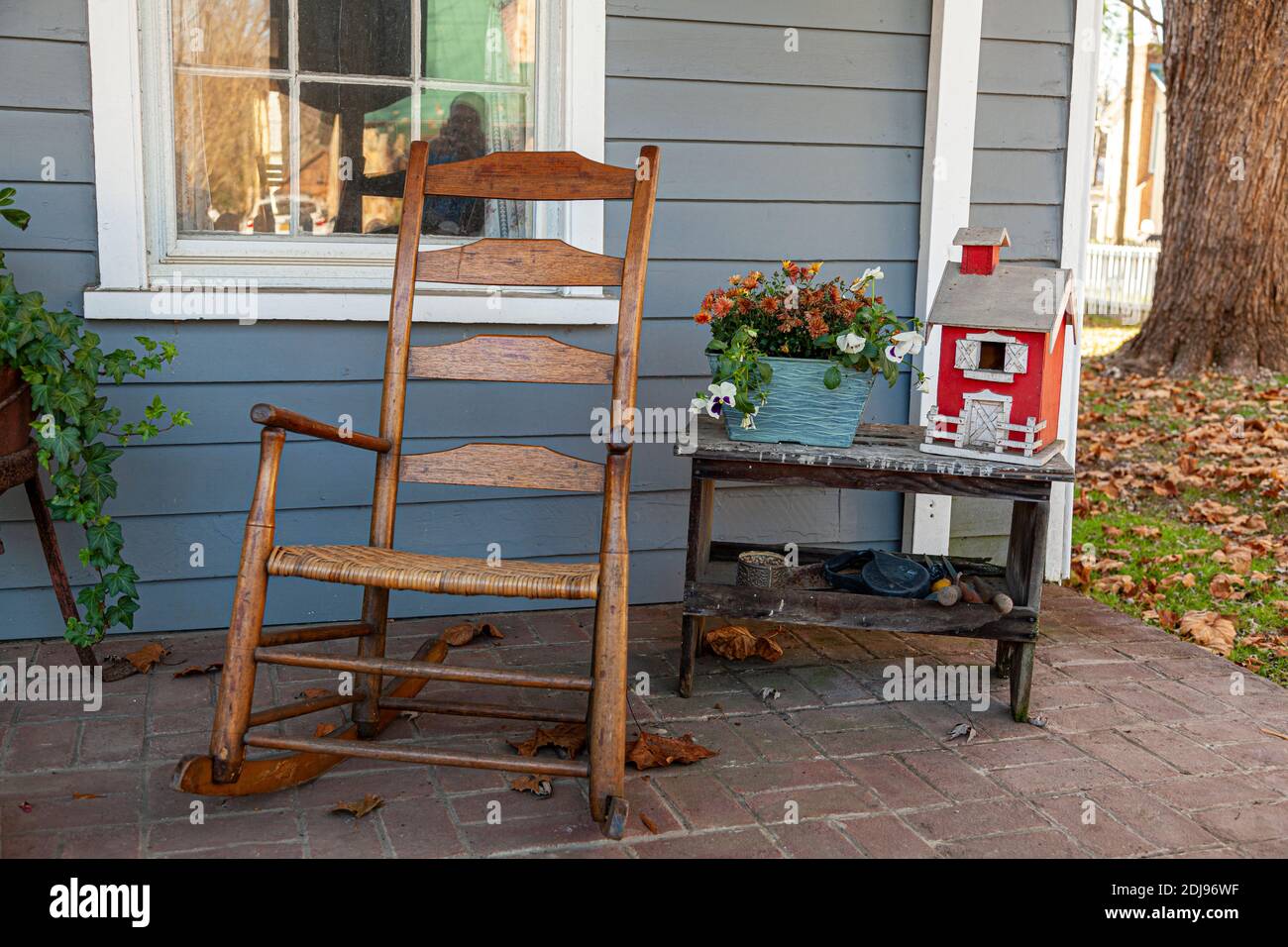 Une décoration de porche dans une maison de l'époque coloniale avec un vieux fauteuil à bascule en bois, une petite table avec des outils de forgeron en métal et une ferme modèle sur t Banque D'Images