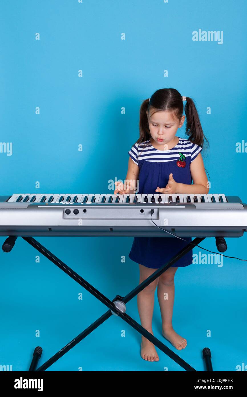 portrait complet d'un enfant triste et déçu refusant d'apprendre à jouer le synthétiseur, vue de face isolée sur fond bleu Banque D'Images