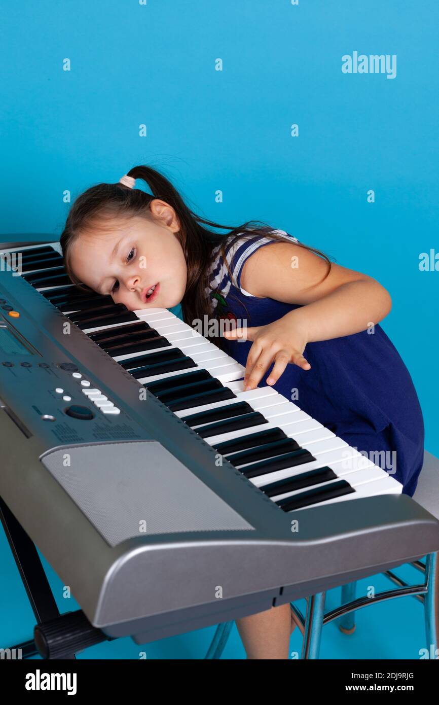 triste fille ne veut pas apprendre à jouer le piano, sa tête est sur les touches du synthétiseur, isolé sur fond bleu Banque D'Images