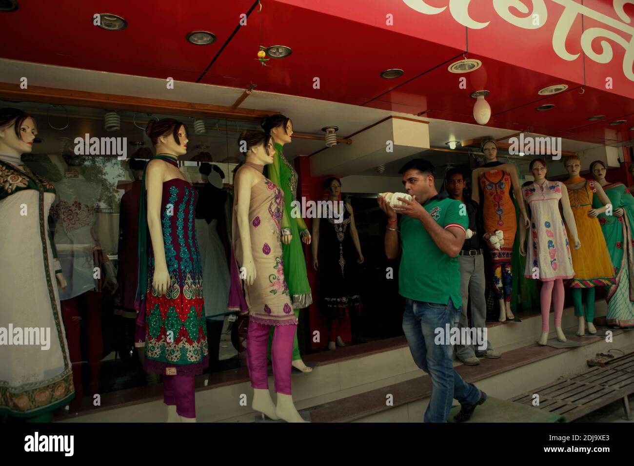Un travailleur marchant devant une rangée de mannequins, alors qu'il est sur le point de remplacer une ampoule à l'avant d'un magasin de mode à Varanasi, Uttar Pradesh, Inde. Banque D'Images