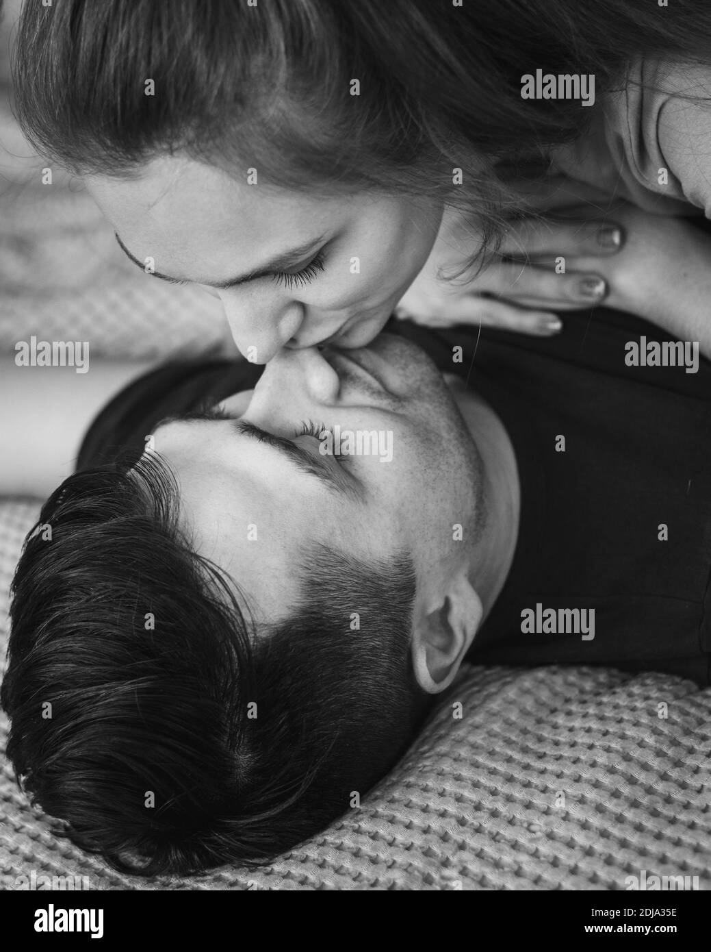 Couple heureux allongé dans le lit ensemble et embrassant à la maison Banque D'Images