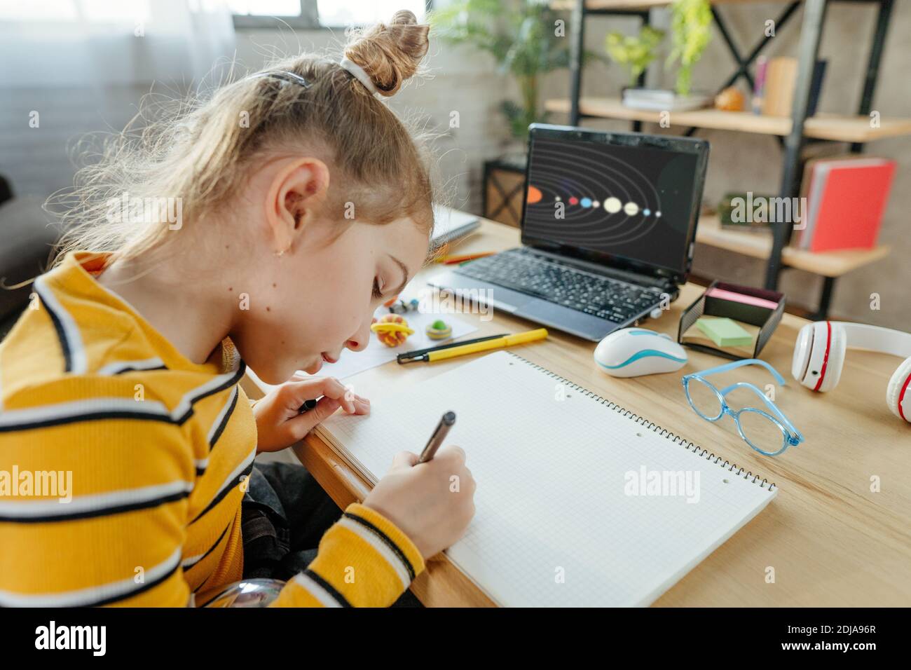 Une fille de 8 ans étudie le système solaire assis au bureau dans la chambre. Une étudiante de l'école élémentaire fait ses devoirs dans le livre d'exercice. Banque D'Images