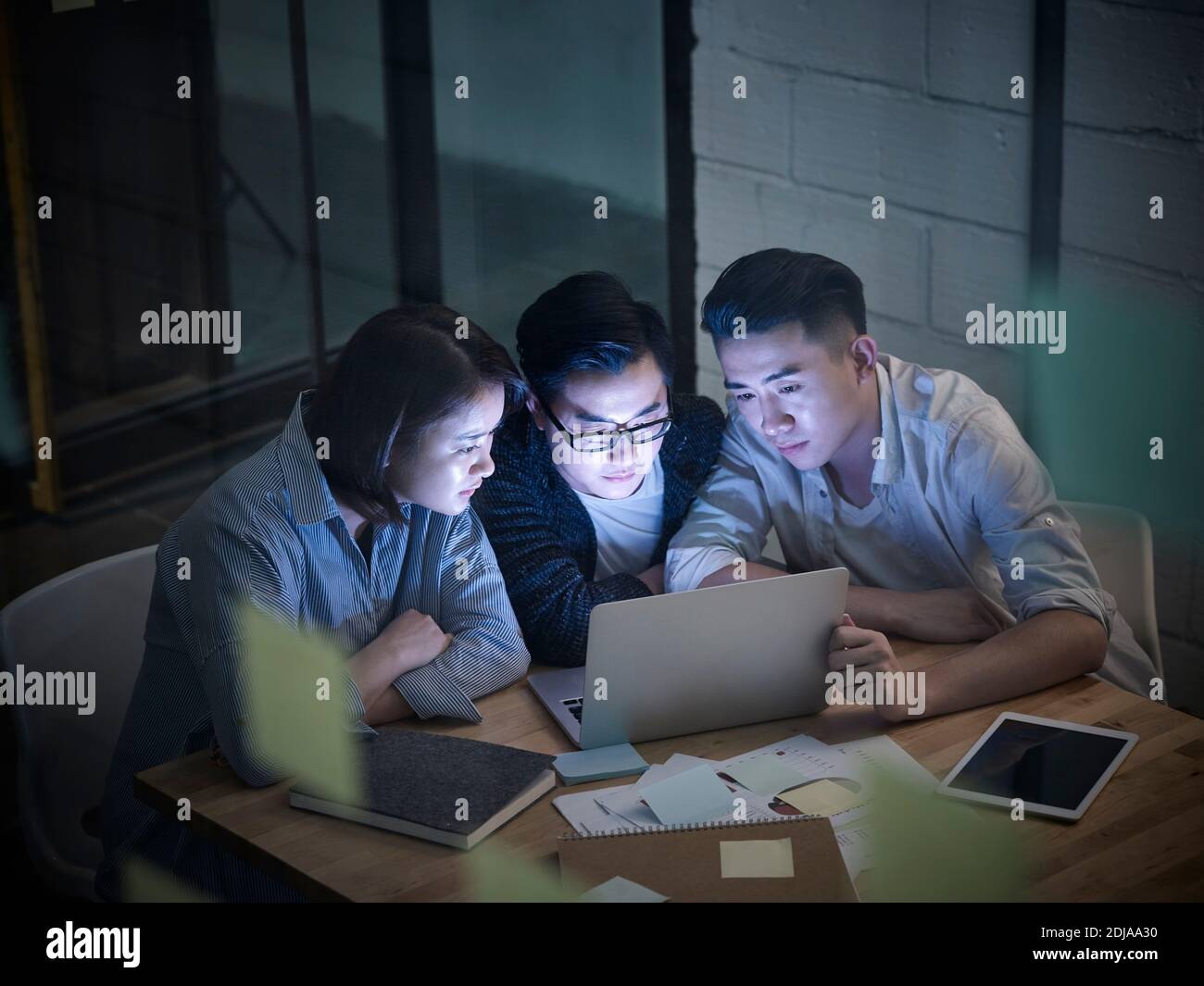 trois jeunes entrepreneurs asiatiques qui travaillent en retard dans une réunion au bureau discutant les entreprises utilisant un ordinateur portable Banque D'Images