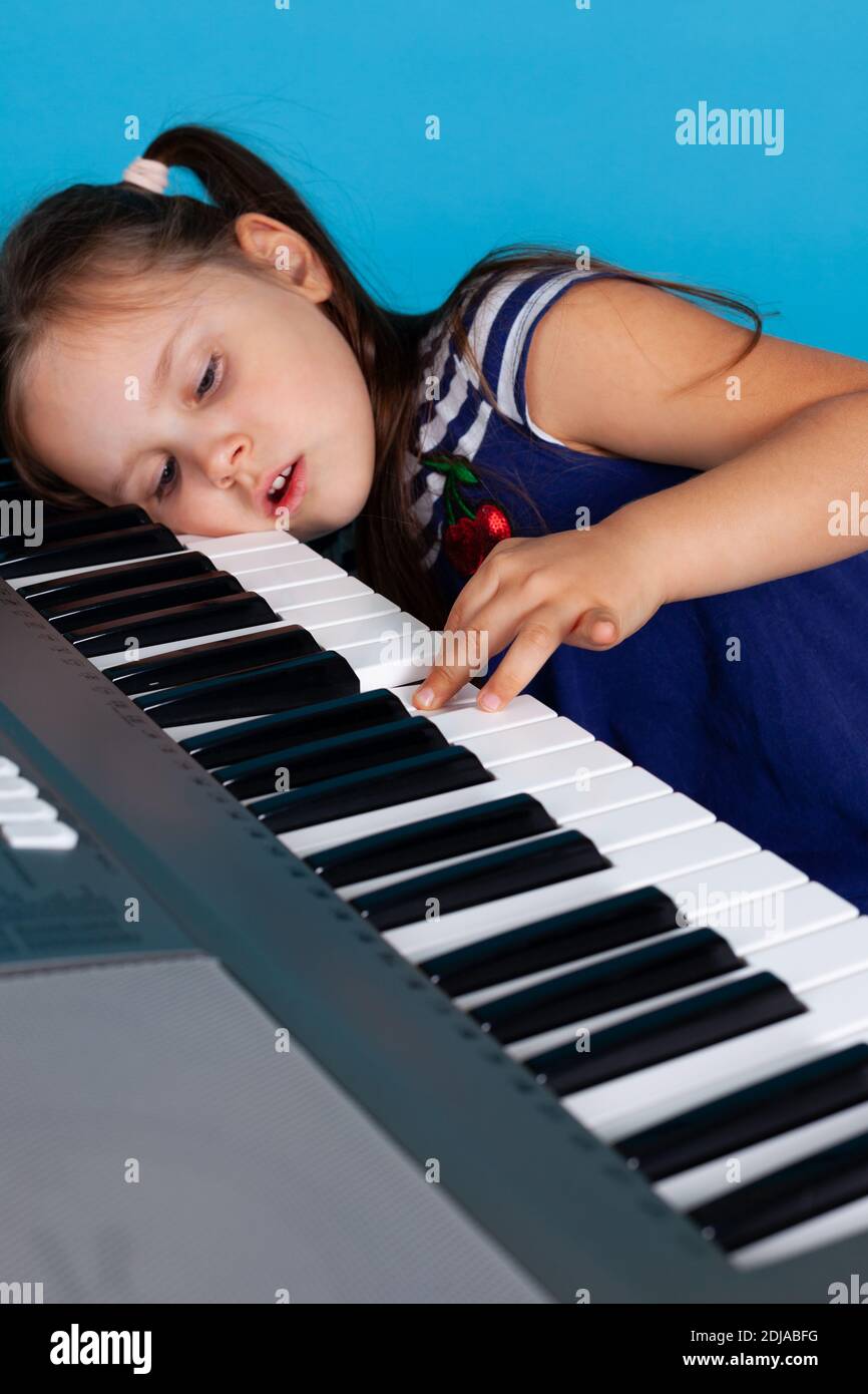 gros plan d'une fille fatiguée avec sa tête sur les touches du synthétiseur, détestant une leçon de musique isolée sur fond bleu Banque D'Images