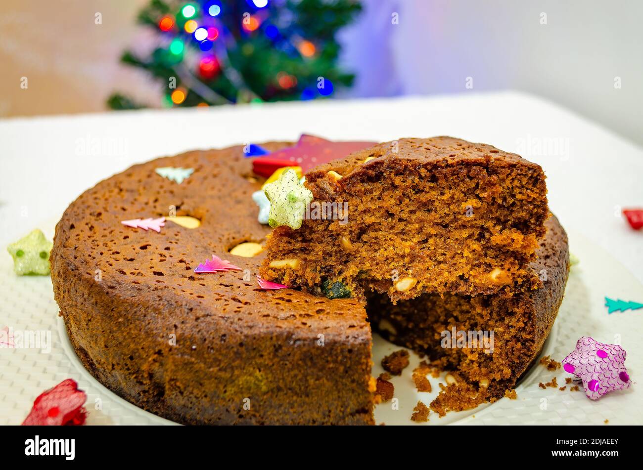 Gros plan d'un gâteau de prune coupé pour les fêtes de Noël. Le gâteau est décoré et un arbre de Noël en arrière-plan. Banque D'Images