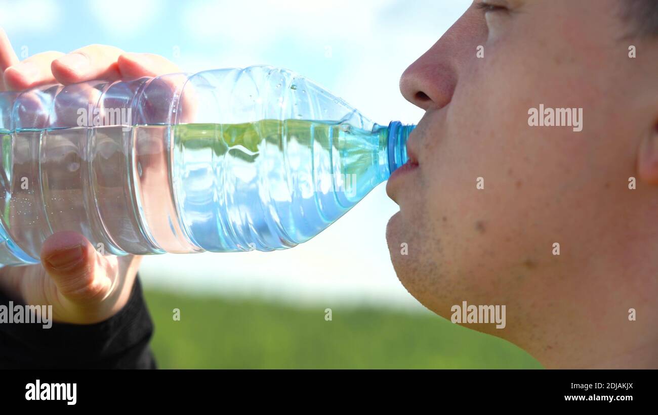 Soif désaltérante. Buvez de l'eau propre dans une bouteille. Un jeune homme d'apparence caucasienne boit de l'eau d'une bouteille en plastique transparent contre un bleu Banque D'Images