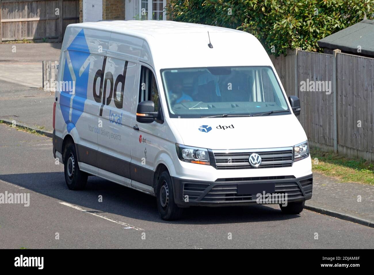 Logo de la marque commerciale sur le côté et à l'avant de VW dpd transport de minibus de livraison de la chaîne d'approvisionnement de colis locale bleue & Chauffeur dans la rue résidentielle Angleterre Royaume-Uni Banque D'Images