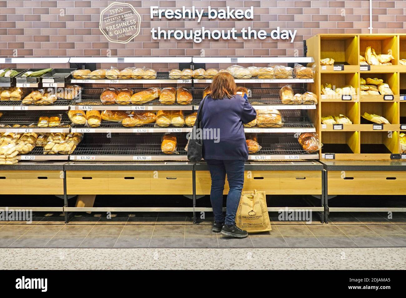 Vue arrière des clients qui magasinent du pain au supermarché Tesco les tablettes de sélection de produits de boulangerie en magasin sous l'affiche pour les produits fraîchement cuits Toute la journée Londres Angleterre Royaume-Uni Banque D'Images