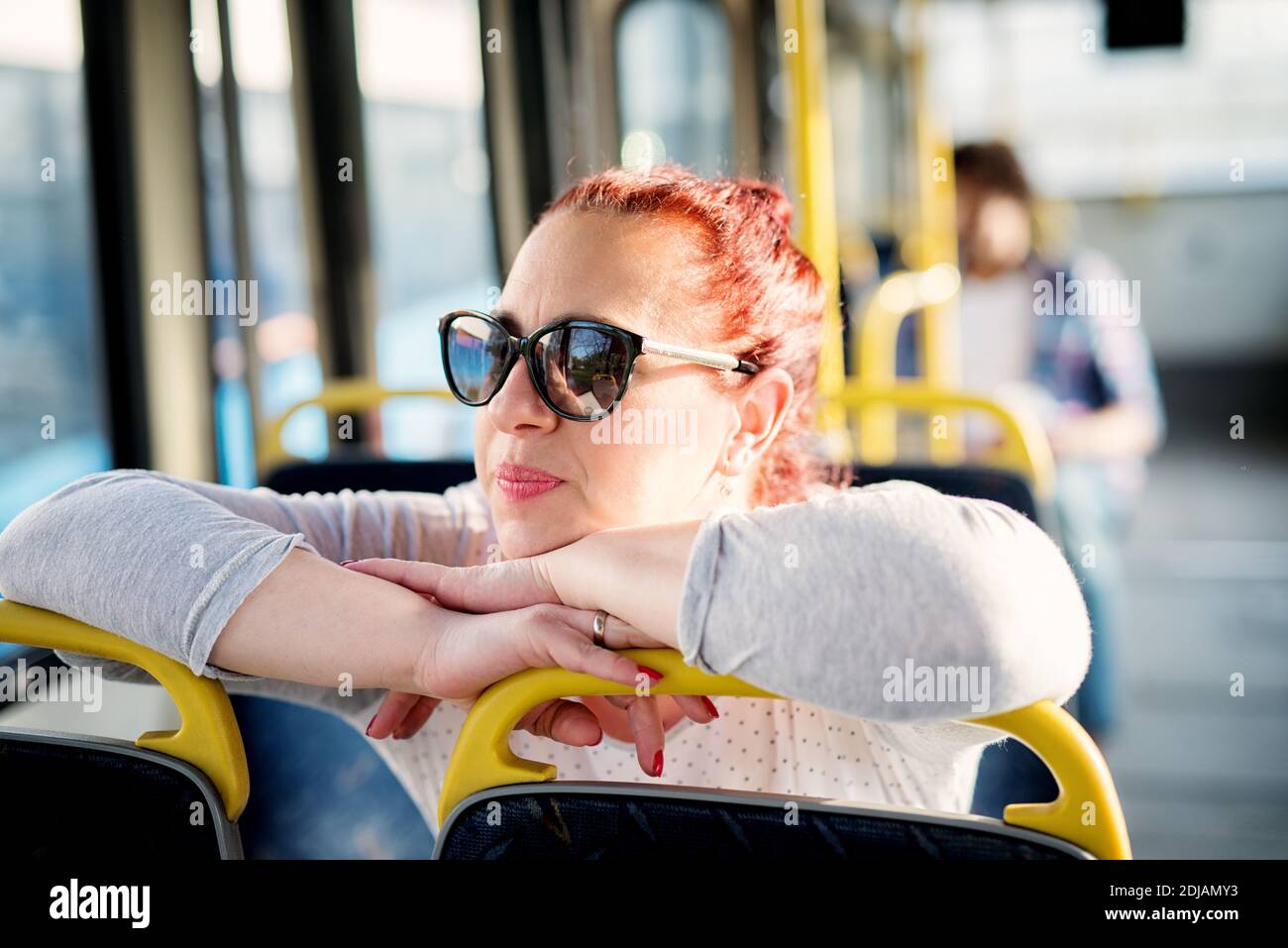 Une femme mûre avec des lunettes de soleil est assise dans un siège de bus et se penche sur les sièges devant elle et regardant par la fenêtre. Banque D'Images
