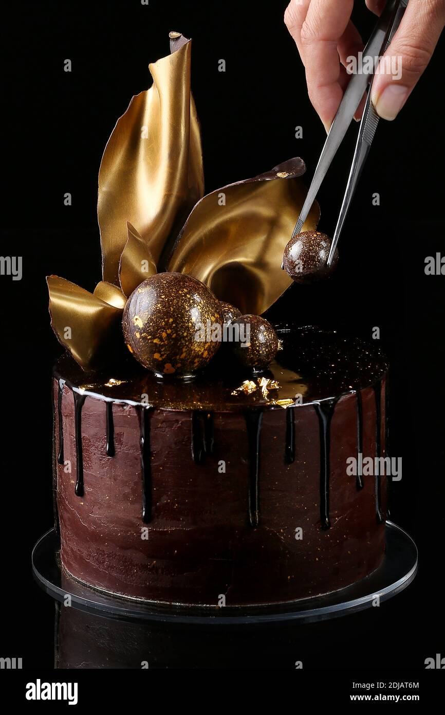 Gâteau au chocolat de fantaisie, isolé, fond noir, studio. La main du chef pâtissier est présente dans le cadre Banque D'Images