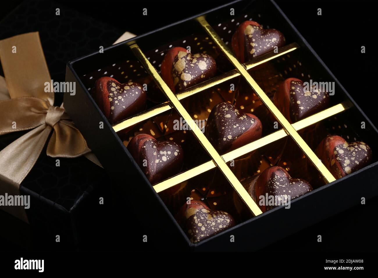 Des bonbons faits main de luxe peints dans une boîte cadeau sur fond noir. Chocolats pour la Saint-Valentin. Banque D'Images