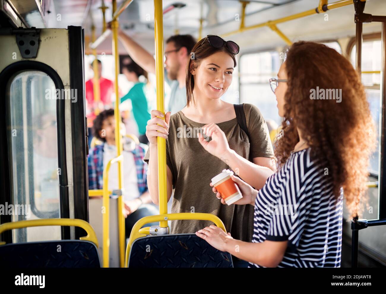 Deux jolies jeunes femmes boivent du café et ont une conversation agréable en étant debout dans le bus. Banque D'Images