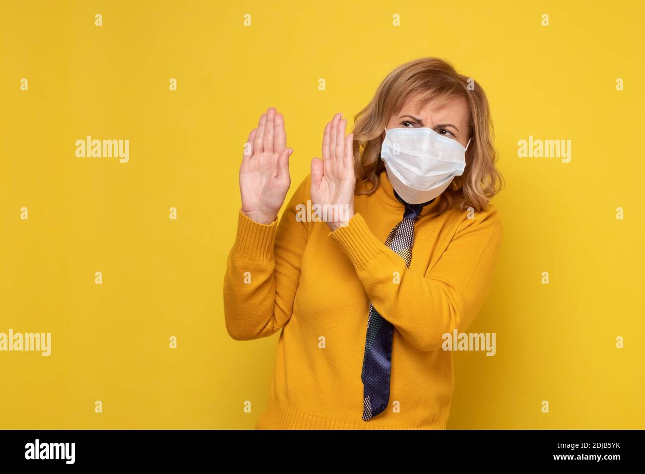 Femme mature dans un masque protecteur pour arrêter l'infection de la maladie corona virus Covid-19. Studio tourné sur un mur jaune. Banque D'Images