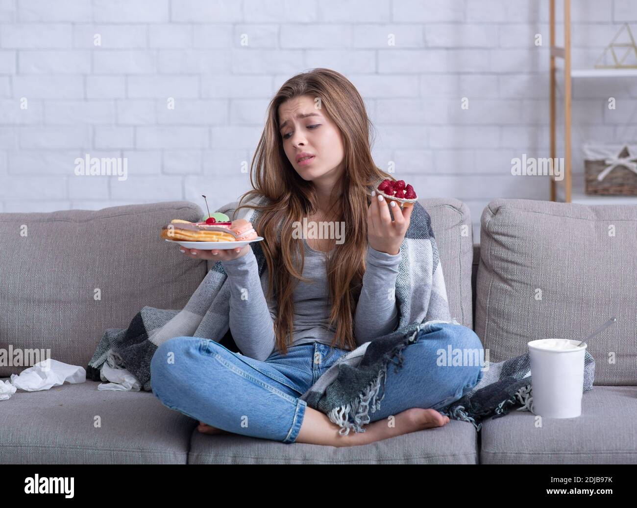 Notion de troubles de l'alimentation. Jeune femme stressée dévorant des bonbons sur le canapé à la maison, portrait pleine longueur Banque D'Images
