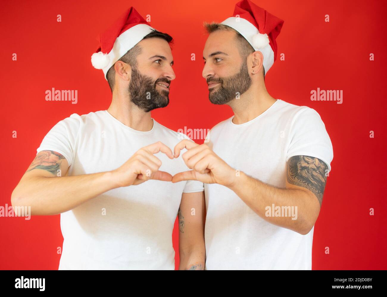 Couple gay heureux en chapeau de père noël et vêtements décontractés,  faisant le coeur de la forme des doigts, portrait de studio sur fond rouge  Photo Stock - Alamy