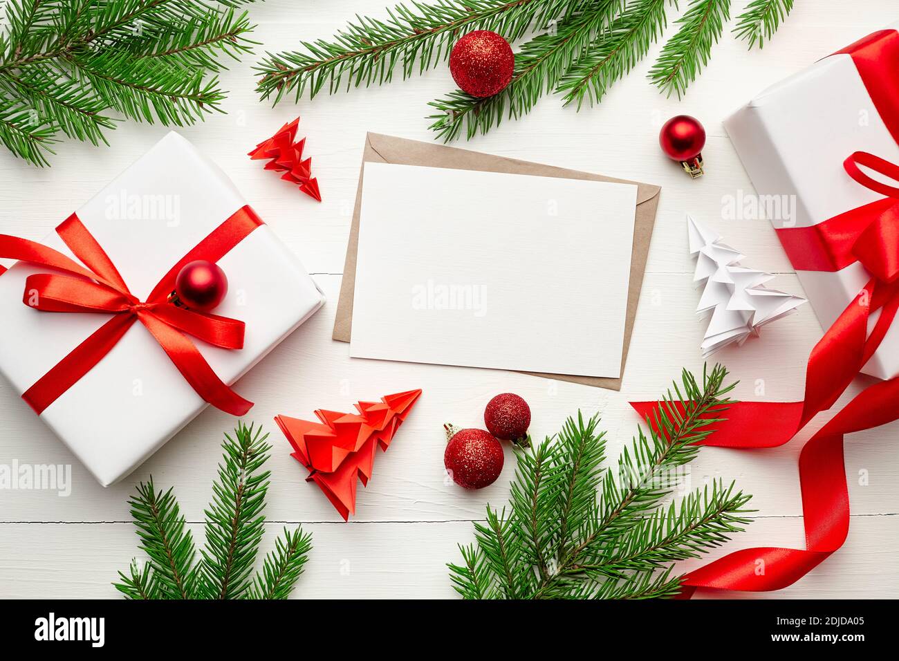 Carte de vœux de Noël maquette avec boîtes cadeaux, décorations et branches de sapin sur fond blanc en bois, plat Banque D'Images