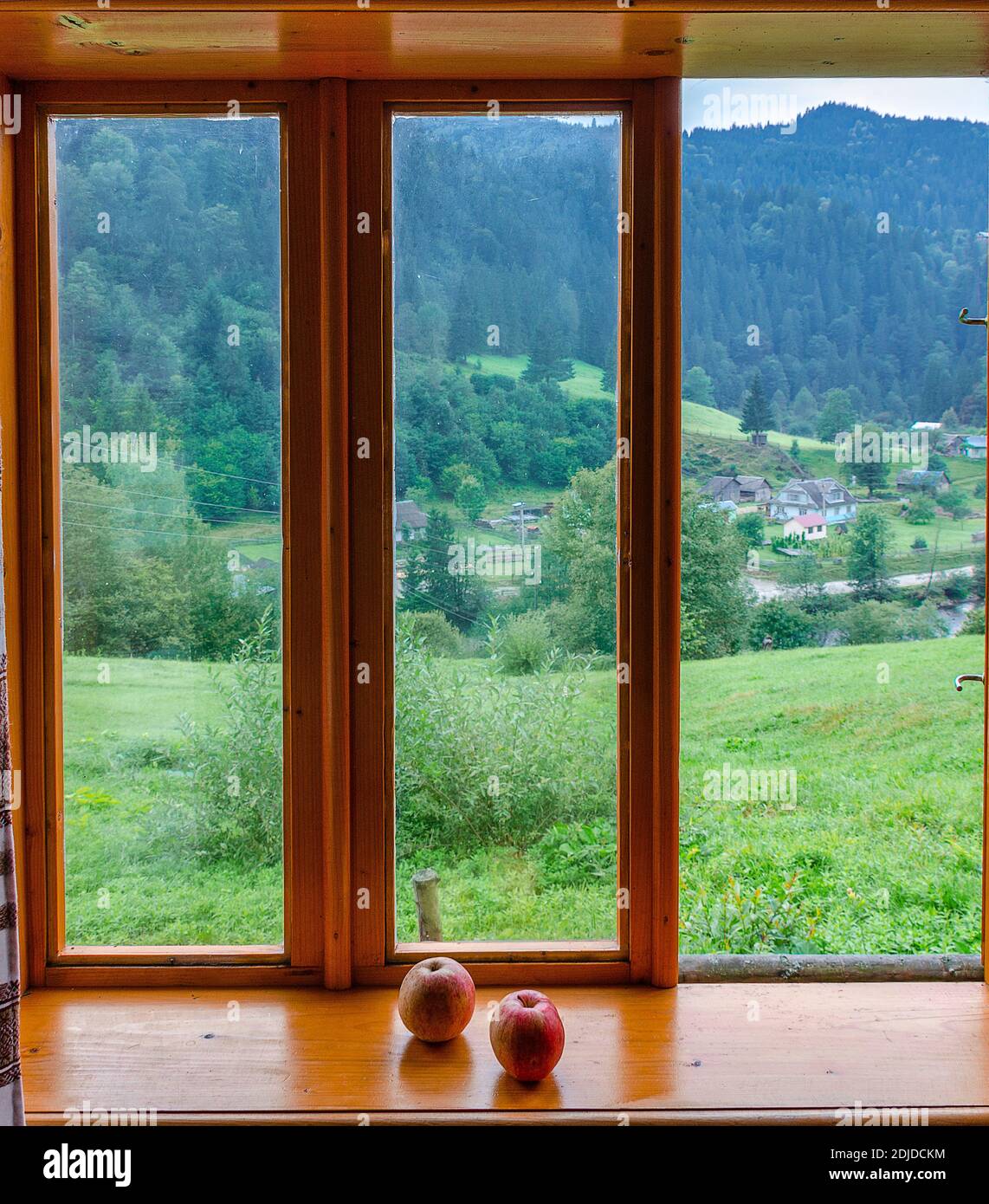 Deux pommes rouges reposent sur un rebord de fenêtre en bois contre la toile de fond des montagnes et de la forêt Banque D'Images