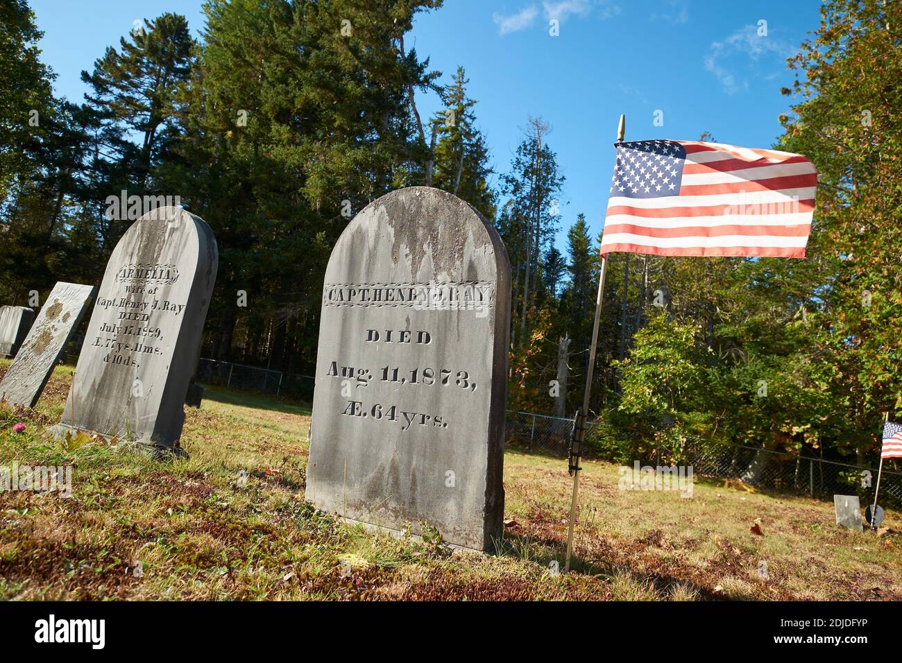 Un drapeau américain vole à côté de la pierre tombale d'un ancien vétéran militaire dans un cimetière rural. Au cimetière de Morgan Bay à Surry, Maine. Banque D'Images