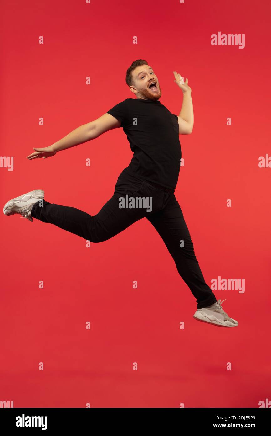 Inspiré. Portrait complet de jeune homme de saut haut réussi gesturant isolé sur fond rouge studio. Modèle caucasien mâle attrayant. CopySpace. Émotions humaines, concept d'expression faciale. Banque D'Images