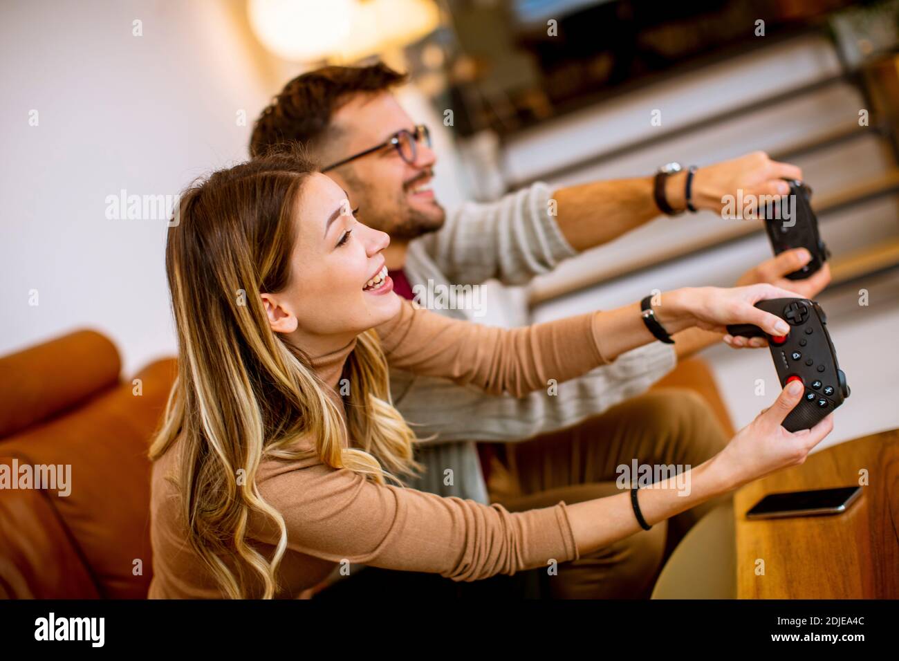 Beau jeune couple jouant à des jeux vidéo à la maison, assis sur un canapé et s'amuser Banque D'Images