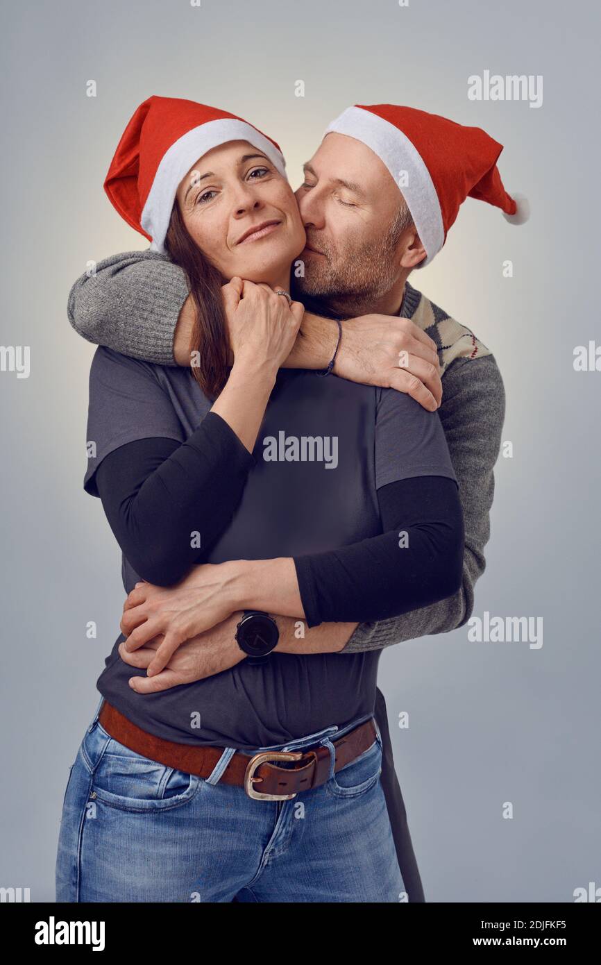 Portrait d'un homme d'âge moyen amoureux embrassant et tenant sa femme, une femme souriante heureuse, tout en portant les deux chapeaux de Père Noël Banque D'Images