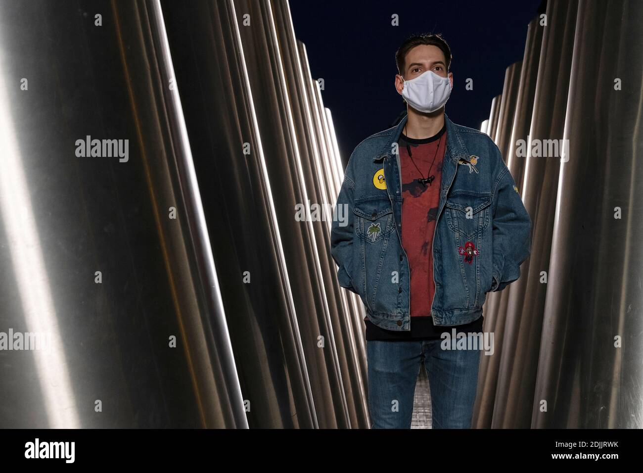 jeune homme avec masque facial et veste en denim se tient entre barres métalliques Banque D'Images