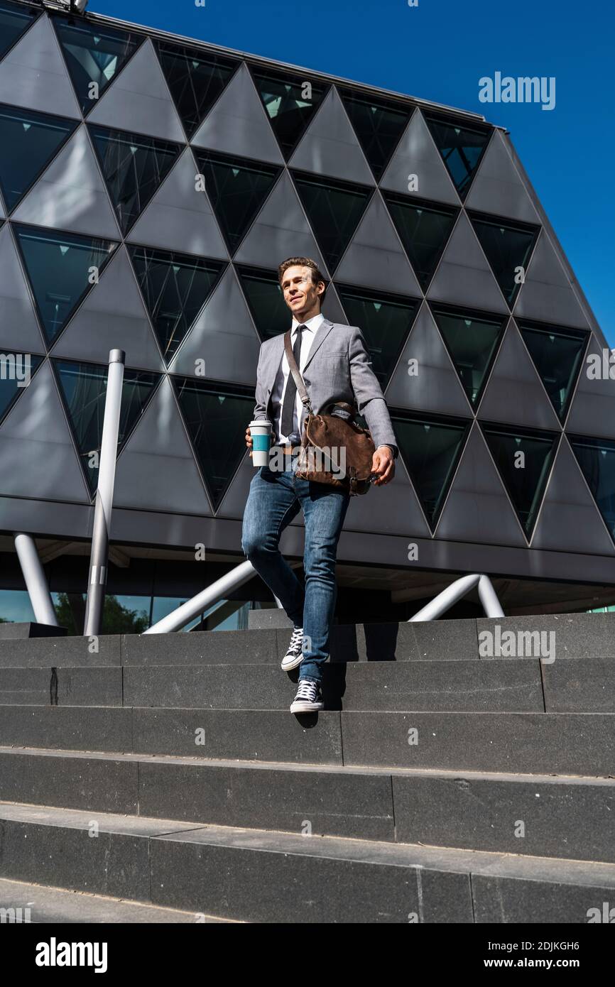 jeune homme avec sac à bandoulière et tasse à café devant de construction d'entreprise Banque D'Images