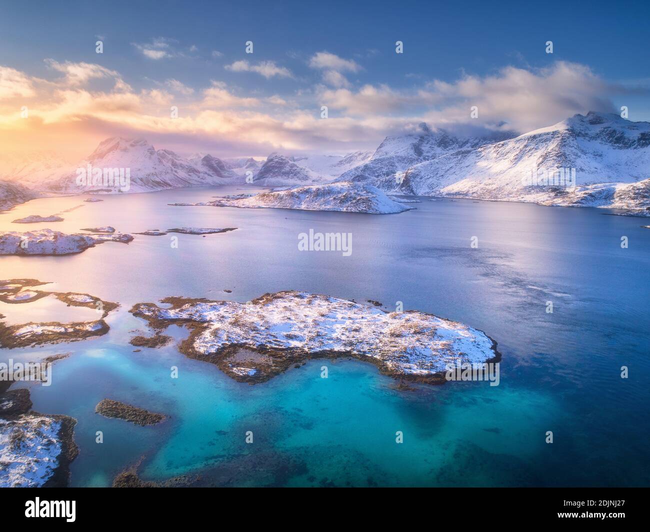 Vue aérienne des îles Lofoten en hiver au coucher du soleil en Norvège. Paysage avec mer bleue, montagnes enneigées, rochers et îles, ciel coloré avec nuages et Banque D'Images
