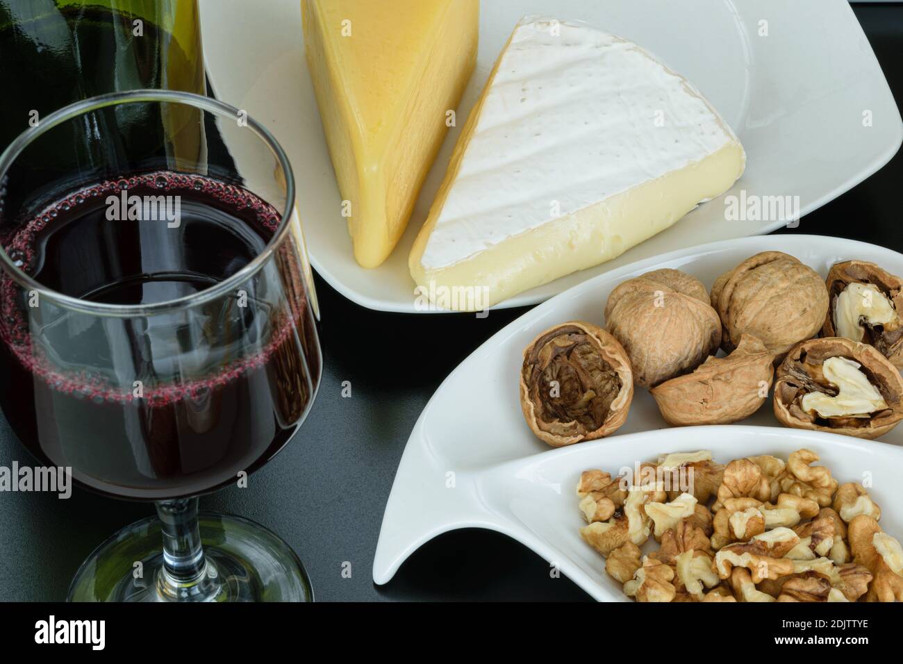 Brie et parmesan accompagnés de noix et d'un verre de vin rouge. Banque D'Images