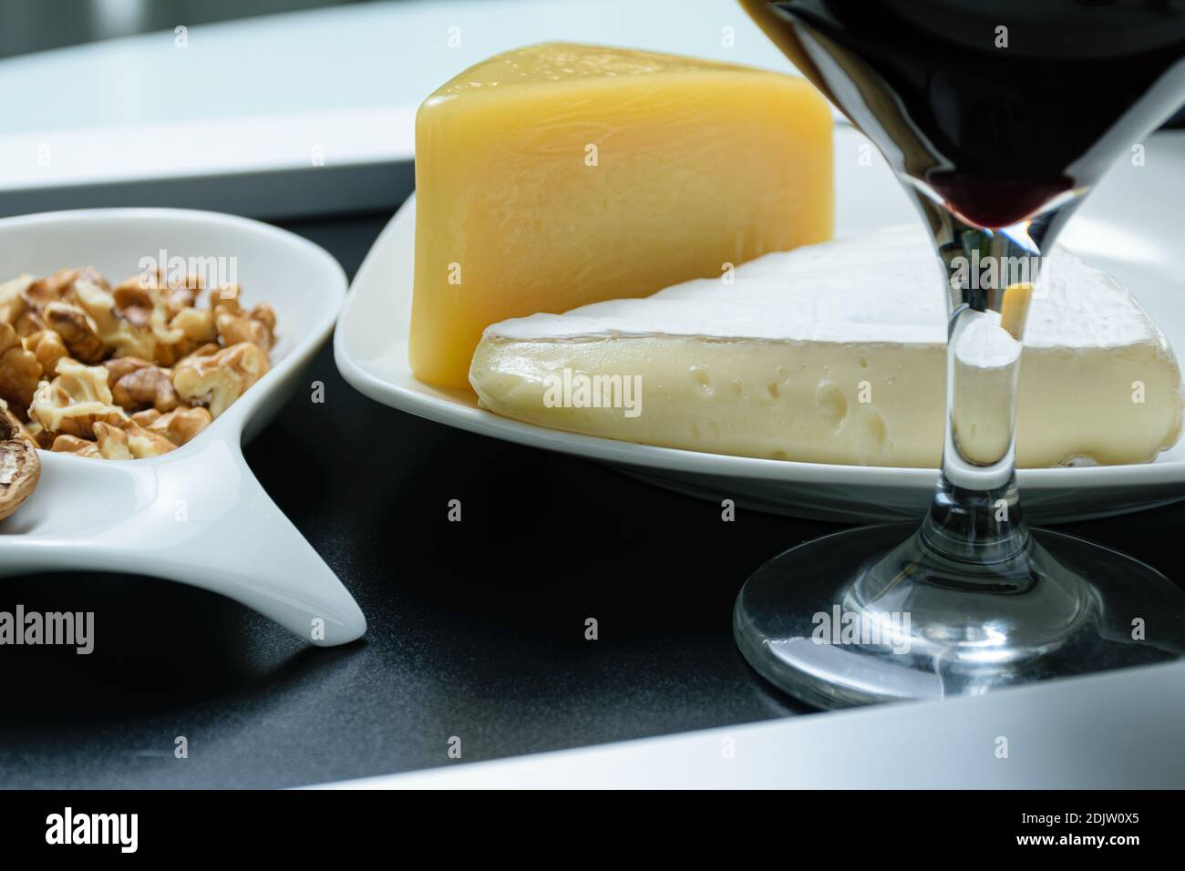 Gros plan sur les fromages brie et parmesan à côté d'une portion de noix et d'un verre de vin rouge. Banque D'Images