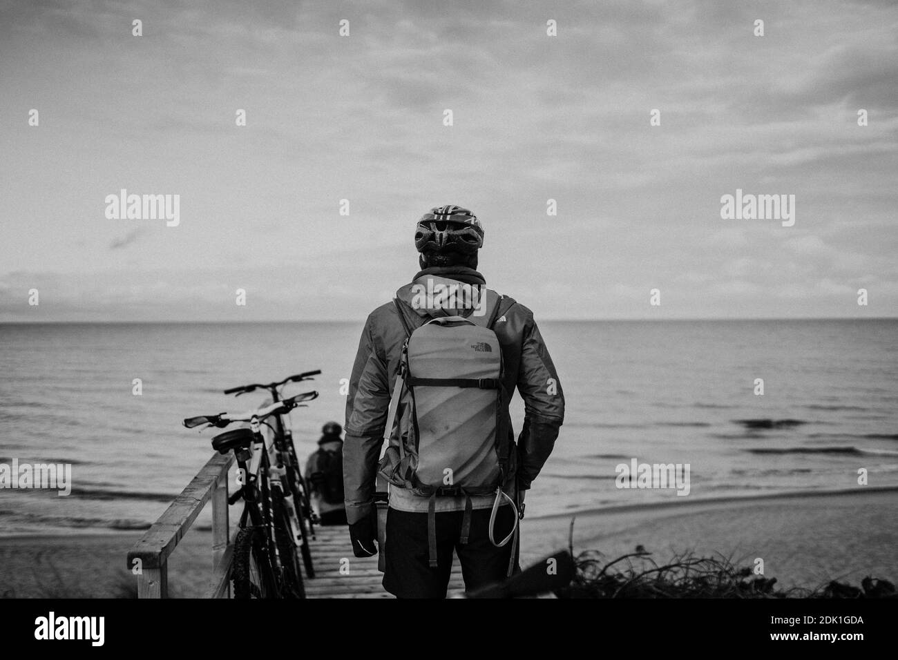 Une belle photo en niveaux de gris d'un homme debout en face du lac. Tourisme avec un vélo sur la plage Banque D'Images