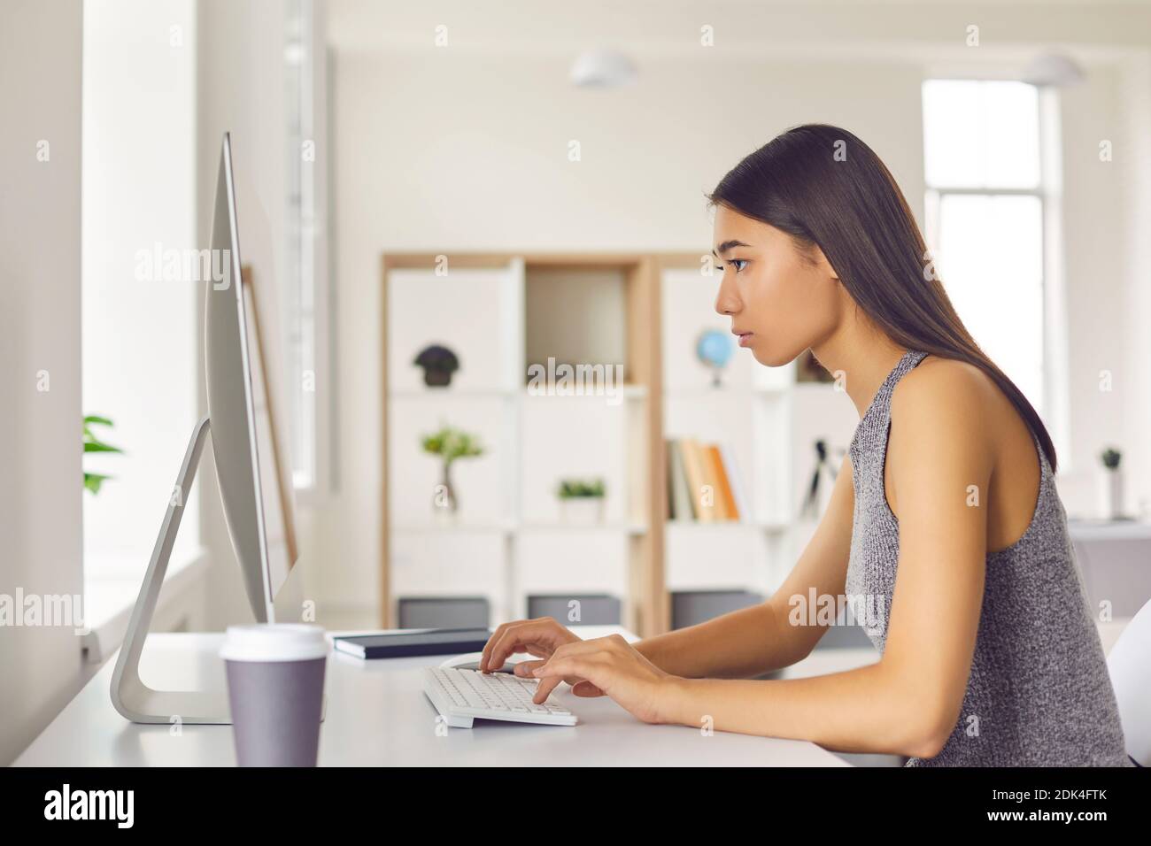 Jeune femme asiatique de bureau travaillant à l'ordinateur et de surveiller et de travailler en ligne, vue latérale Banque D'Images